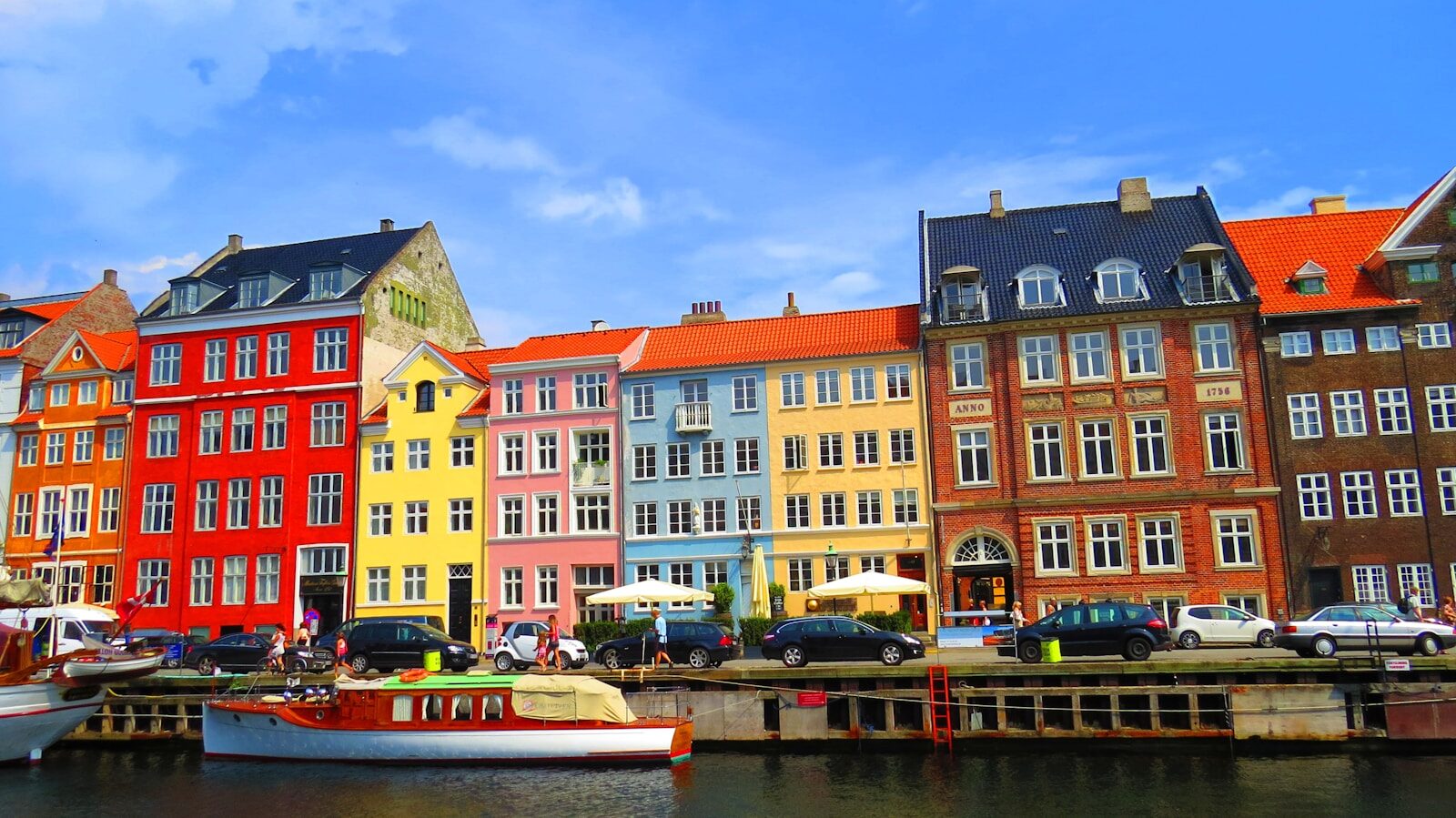 Colorful buildings line a canal with boats and cars.