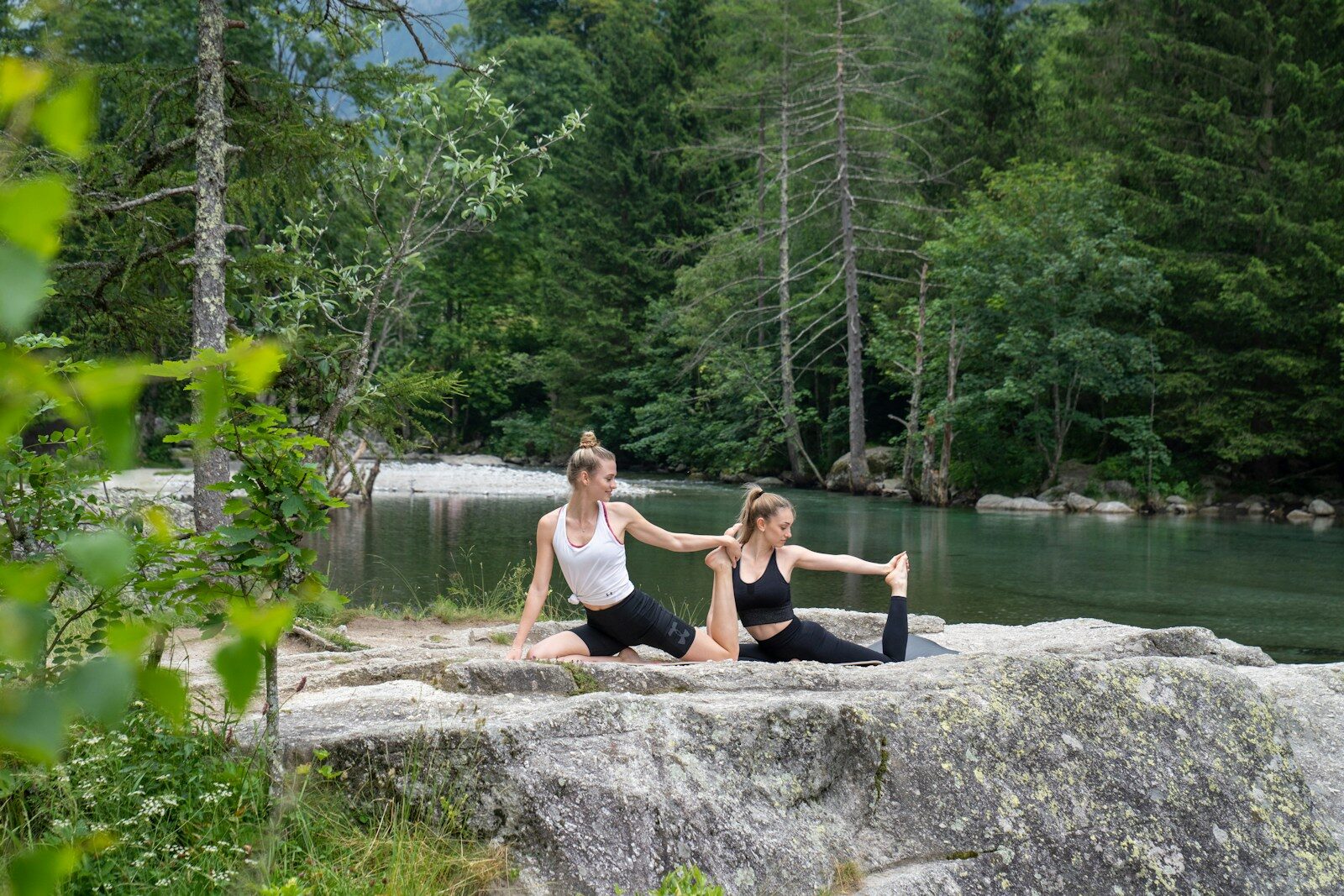 two women doing yoga on a rock near a river